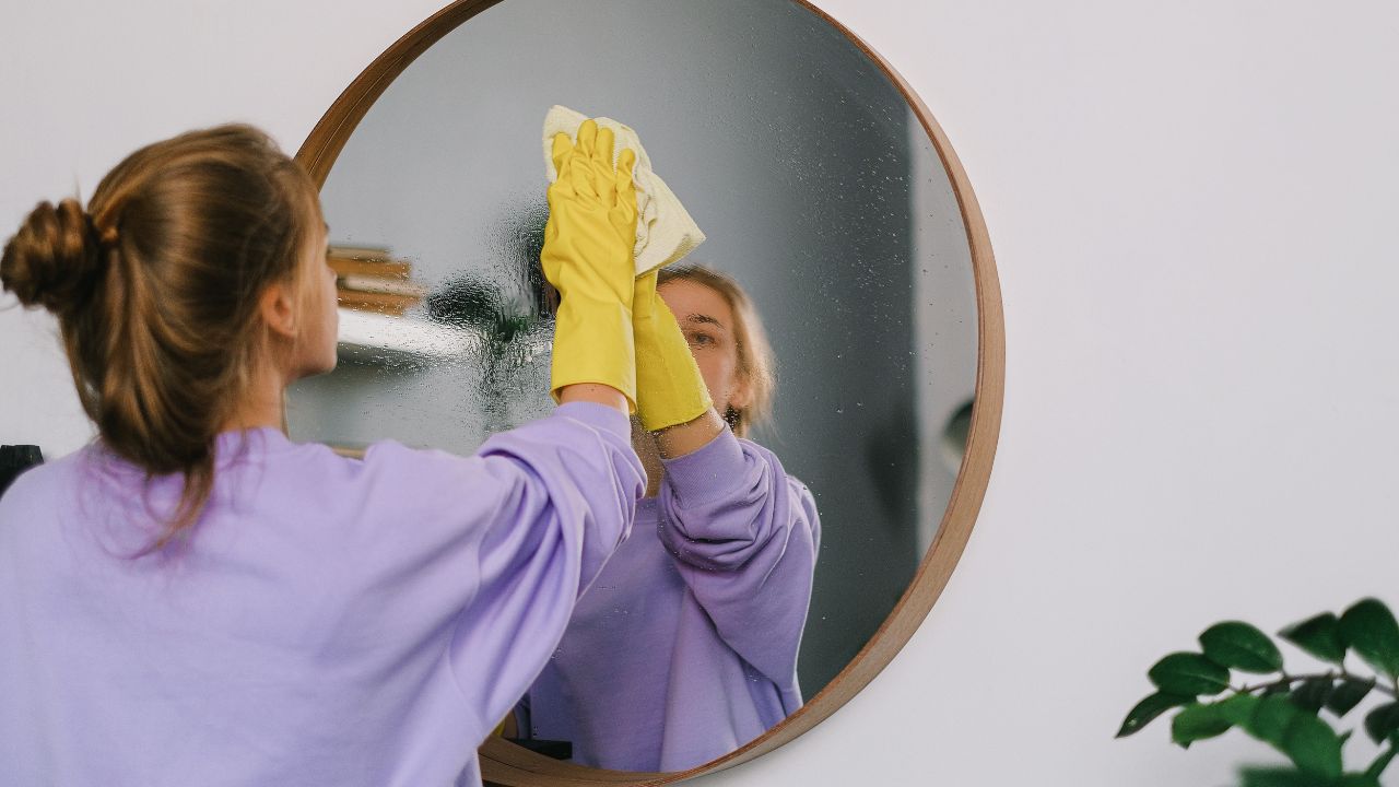 Person wearing a purple sweater and yellow gloves wiping down a circular mirror